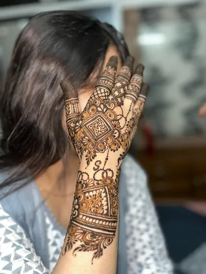 A beautiful example of a geometric henna design. This style features sharp lines, checkerboard patterns, and delicate chains, with the initial 'S' hidden in the artwork for a personal touch.