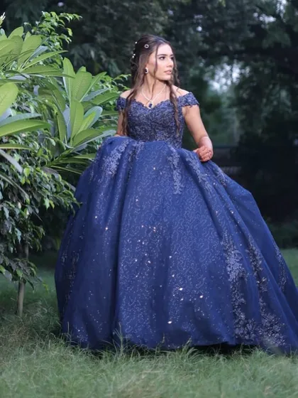 A candid shot of the bride-to-be during her engagement photoshoot. Her makeup features a soft, romantic palette that enhances her features without overpowering her intricate navy blue gown, perfect for the garden setting.