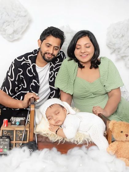 A sweet family portrait with their sleeping newborn. Our dreamy cloud setup, complete with teddy bears and a tiny bed, creates a whimsical and peaceful scene.