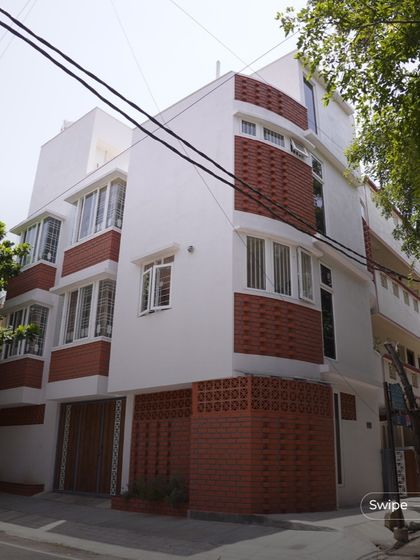 A full view of the Gopal Residence, a multi-story urban home that uses projecting bay windows and terracotta accents to create a dynamic and modern elevation.