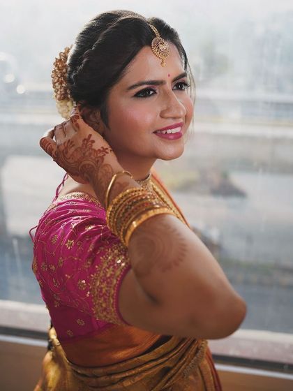 A happy bride glowing on her wedding day. This close-up shows her fresh and radiant makeup, with a bright smile and sparkling eyes. The traditional hairstyle adorned with flowers adds a classic South Indian touch.