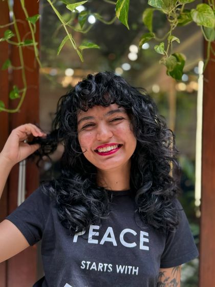 Curly bangs are the cutest! This client is radiating joy with her new fringe and layered cut that perfectly frames her smiling face.