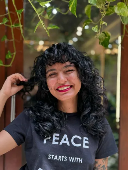 Curly bangs are the cutest! This client is radiating joy with her new fringe and layered cut that perfectly frames her smiling face.
