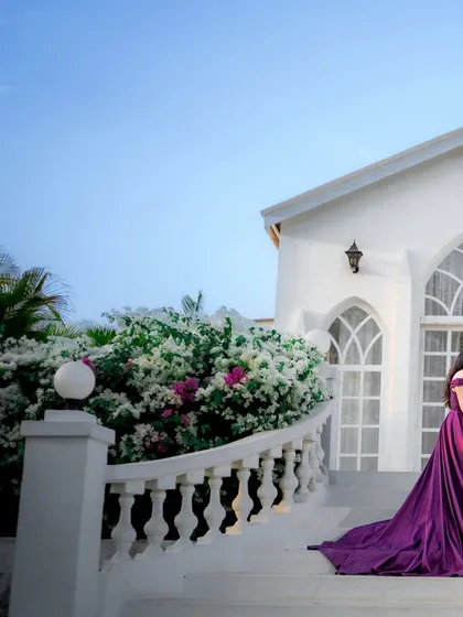 The bride's vibrant purple gown stands out against the white architecture and clear blue sky, creating a striking and beautiful pre-wedding photograph.