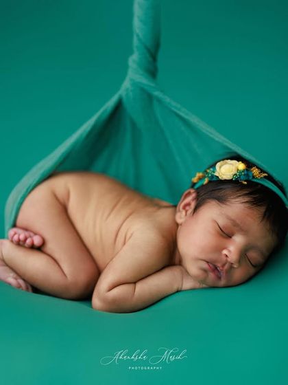 This pose, with the baby gently supported in a sling, mimics how they were in the womb. The rich teal color provides a beautiful, deep background that makes the baby stand out.