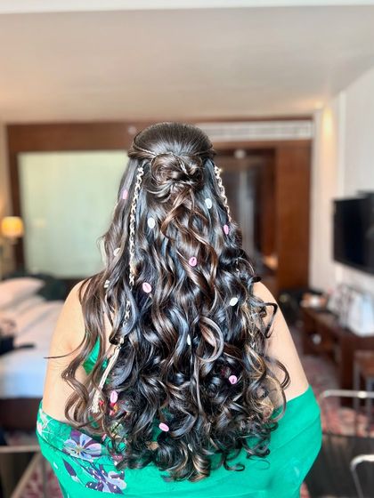 A playful 'carnival' look featuring a half-up bun, multiple small braids, and bouncy curls, adorned with delicate floral accessories.