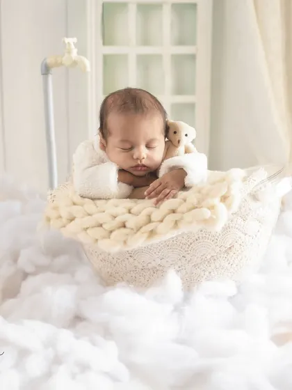 A dreamy bubble bath scene, without any water. The baby sleeps peacefully in a basket filled with soft blankets, surrounded by fluffy clouds and rubber ducks.