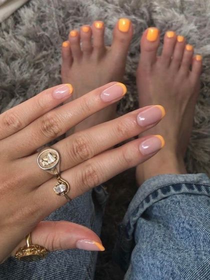 A matching mani-pedi with orange French tips on the hands and solid orange on the toes.