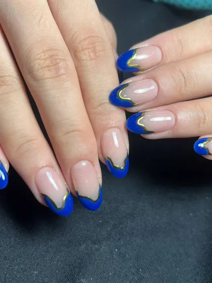 A modern French manicure with bold royal blue tips and a liquid gold chrome outline.