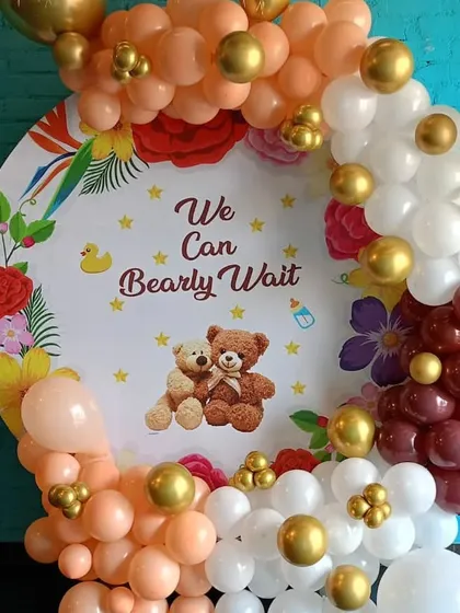 A warm and inviting "We Can Bearly Wait" baby shower theme. The round backdrop is framed by a beautiful balloon arrangement in peach, white, burgundy, and gold.