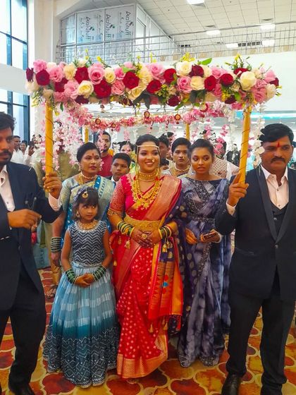 This bride is entering her wedding ceremony under a beautiful chadar decorated with pink and red roses, perfectly complementing her traditional red saree.