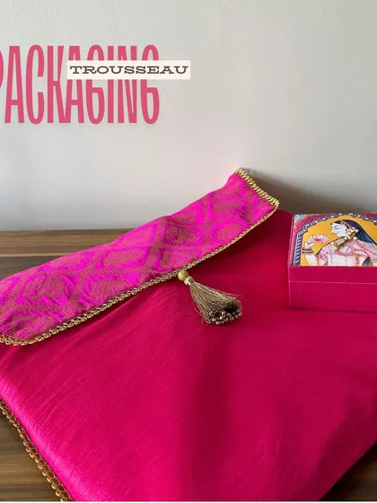 This image focuses on the packaging elements of the trousseau. A beautiful saree cover and a matching jewelry box in rani pink create a coordinated and luxurious gifting presentation.