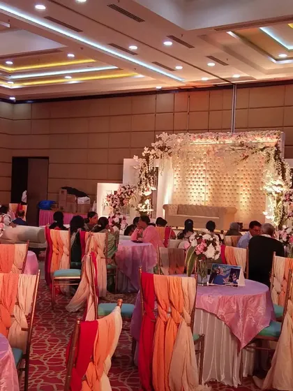 A pastel-themed indoor event with a focus on seating. The tables are covered in multi-colored pastel linens, and the chairs are decorated with flowing organza sashes in shades of peach and pink.