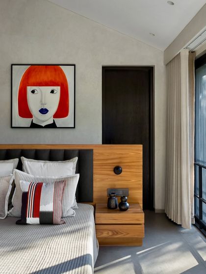 This bedroom in the Mango Orchard House features a bold piece of contemporary art that contrasts with the calm, textured walls and warm wood of the integrated headboard.