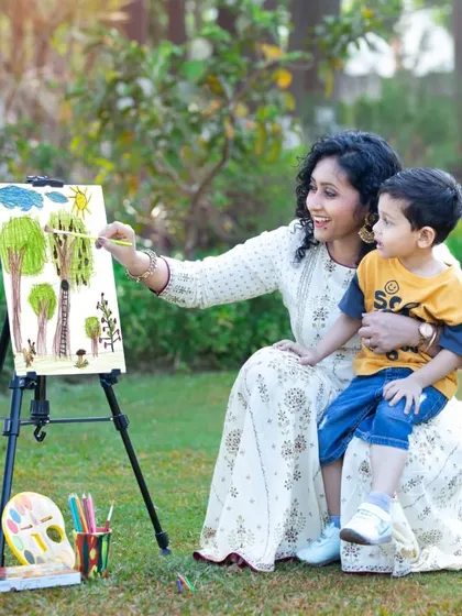 A mother guides her son's hand as they paint a picture together.