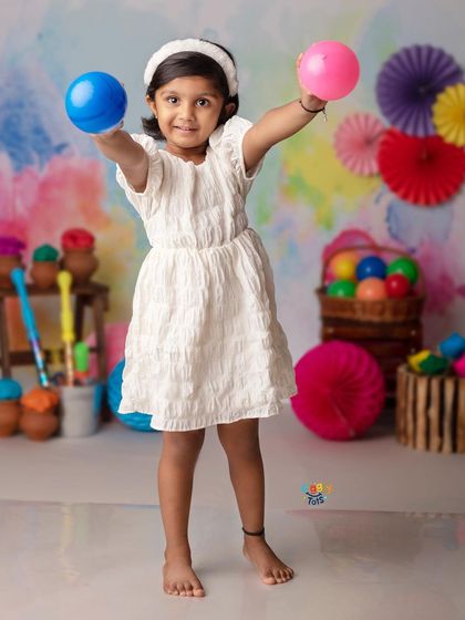 A happy girl holds up colorful balls, ready to play and celebrate the festival of Holi.