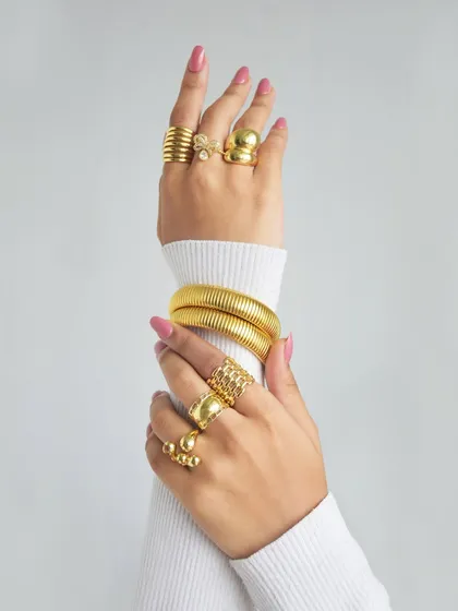 POV: you're setting trends with every layer. This image shows a perfectly manicured hand stacked with our sparkle bow, cuddle, and abstract spiral rings, paired with a chunky bangle.