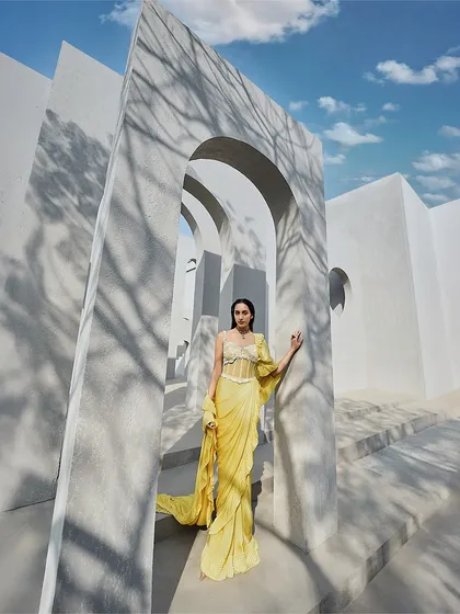 This yellow pre-draped sari gown features a corseted bodice and a flowing ruffle drape, blending playful movement with sculpted form.
