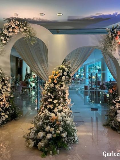 A beautiful and modern entrance created with a series of white arches of varying sizes. Each arch is asymmetrically decorated with cascades of white flowers and greenery, creating a dynamic and elegant passageway.