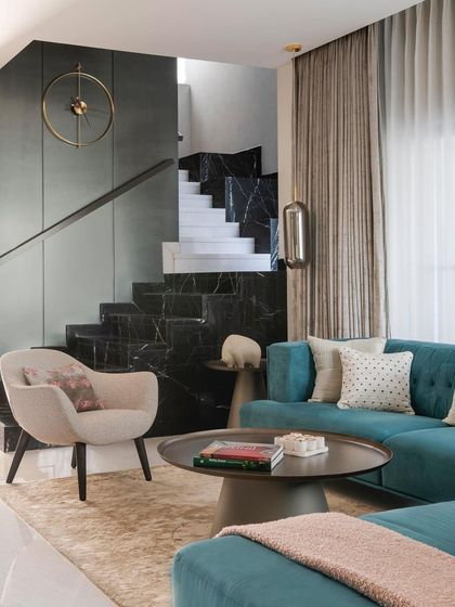 In the 'ARR' residence, we used a bold teal sofa to inject color against a backdrop of dark marble and textured grey walls. The staircase itself becomes a sculptural element, showcasing our use of contrasting materials to create visual interest and define the living space.