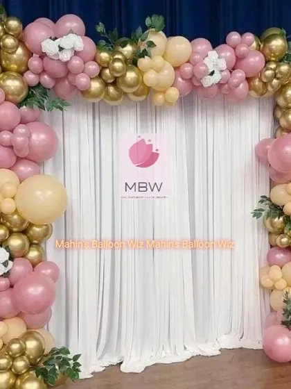 A beautiful balloon arch in shades of dusty rose, cream, and metallic gold. This elegant design is accented with greenery and white flowers, making it perfect for an engagement or reception.