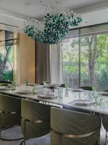 A dining room should be a place for connection. Here, we framed the garden view with floor-to-ceiling windows and brought the tones of nature inside with olive green chairs. The sculptural chandelier and marble table create an elegant atmosphere for memorable meals.