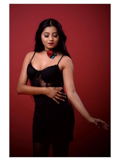 A full-body shot of a model in a glamorous black outfit. The pose is powerful and confident, set against a rich red background for maximum impact.