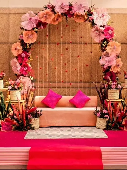 This elegant stage decor uses large paper flowers to create a beautiful arch. The pink and peach color palette, combined with the raised platform and plush seating, makes it ideal for a roka or sangeet ceremony.