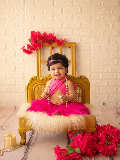 A glamorous birthday girl in a bright pink outfit, posing on a miniature golden chaise lounge.