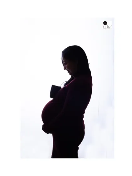 A quiet, contemplative silhouette portrait of a mother-to-be looking down at her bump, a cup in hand, capturing a moment of reflection.