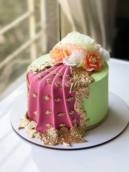 An elegant cake designed for a mehendi function, featuring a fondant saree drape in pink and green with intricate gold detailing.