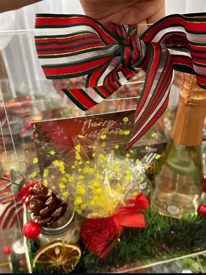 Holding one of our acrylic Christmas hampers, showing the careful arrangement of wine, candles, and treats inside.