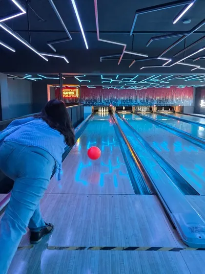 Feel the energy of our neon-lit bowling alley. This is a perfect wide-angle view of the action, showing a player about to release the ball down the glowing lane, ready for that satisfying strike.