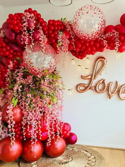A luxurious red balloon arch intertwined with pink cherry blossoms and a 'Love' foil balloon, ideal for Valentine's or an anniversary.
