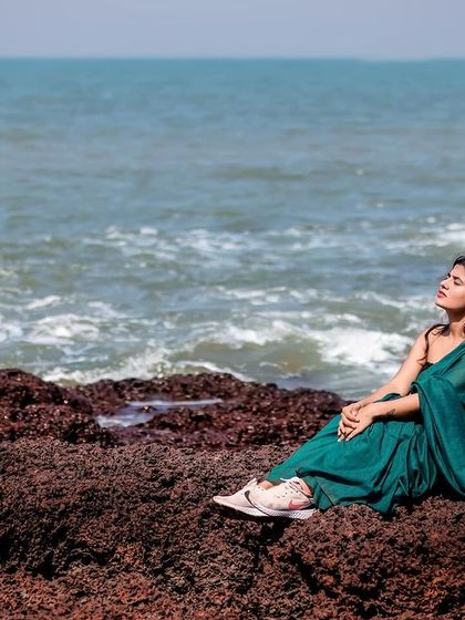 A modern take on saree styling. The model wears a teal saree paired with a contemporary black top, shot in a cafe with earthy tones. This shows how traditional wear can be styled for a modern, chic look.