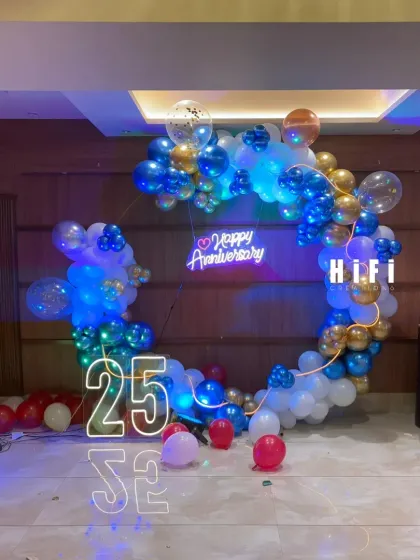 Celebrating 25 years of love with this stylish anniversary decoration. The setup includes a custom heart-shaped balloon arrangement in blue, white, and gold, a "Happy Anniversary" neon sign, and a large light-up number '25' for a truly memorable milestone.