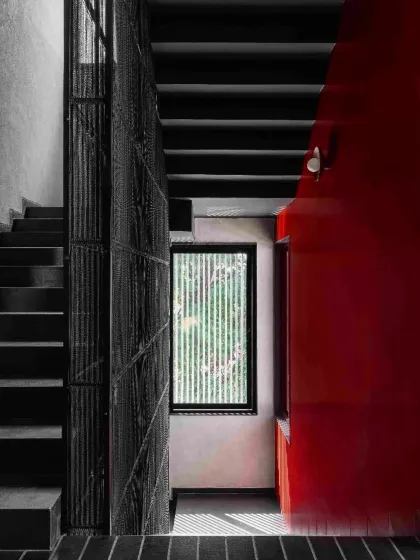 A staircase detail in Project 1374, where a bold red wall contrasts with the dark, textured metal screen and concrete steps. The composition is a study in material, color, and geometric form.