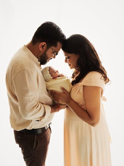 A classic family pose, with mom and dad looking lovingly at their newborn. The neutral outfits create a soft and timeless aesthetic.