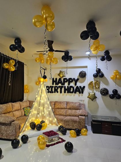 A simple yet elegant 40th birthday home decoration with black and gold balloons and a lighted cabana tent.