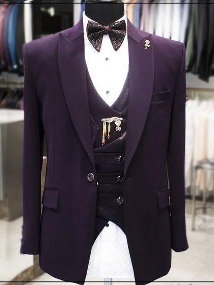 A three-piece tuxedo in a rich wine color, complete with a matching bow tie and lapel pin. The waistcoat adds an extra layer of formality and style.