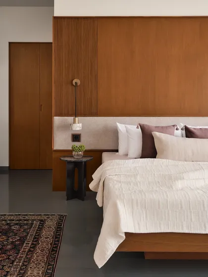 This bedroom at the Amaiti Farmhouse combines a rich wood-panelled headboard wall with soft, neutral bedding. The design is intentionally simple, using a traditional rug and a small, sculptural side table to add layers of personality without clutter.