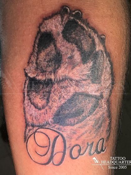 A realistic tattoo of a dog's paw print with the name "Dora," a loving tribute to a furry friend.