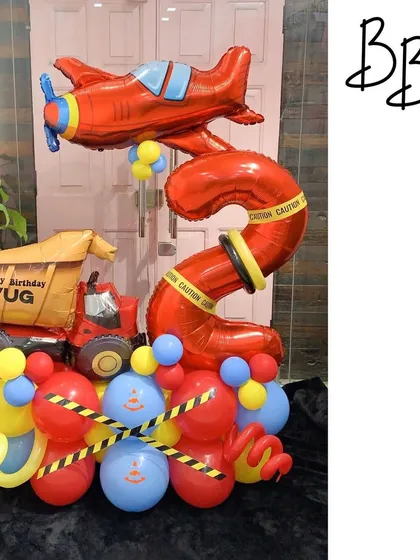 Welcome to the construction party zone! This arrangement for a 5th birthday is perfect for a little one who loves trucks and planes, featuring a dump truck, an airplane, and caution tape details.