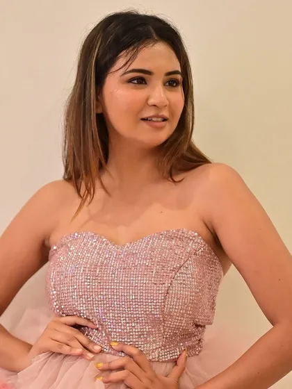 A close-up of a model in a playful, tiered pink dress. The makeup is youthful and fun, with a shimmery eyeshadow and a glossy lip.