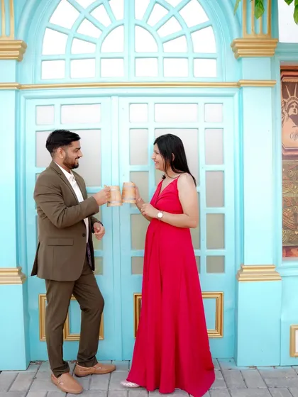 A playful moment sharing a drink against a vibrant blue door, reminiscent of a European street. The woman's bright red dress pops against the cool tones, creating a lively and stylish pre-wedding photo.
