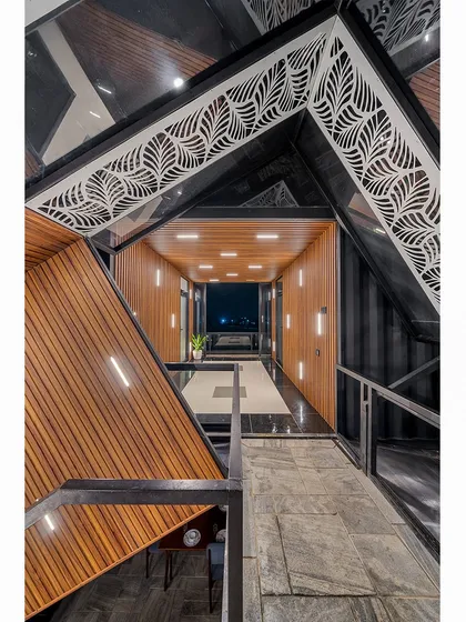 The interior corridor of the container home, where industrial structure meets refined design. The intricate laser-cut metalwork and warm wood paneling create a stunning contrast of materials and textures.
