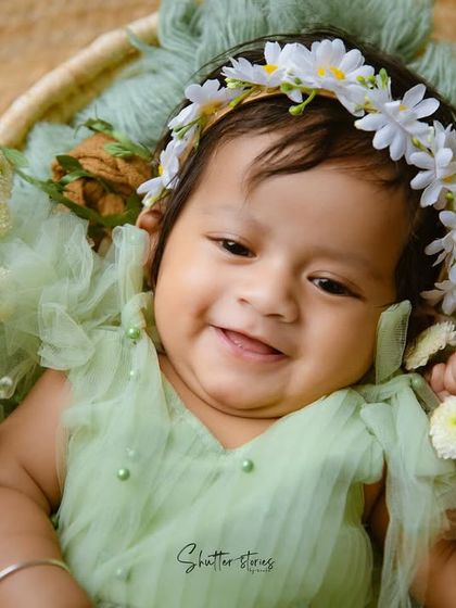 A heart-melting smile from this sweet baby girl, holding a little white flower.