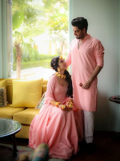 A serene portrait of a couple in matching pink outfits for their haldi ceremony, set in a beautifully lit room.
