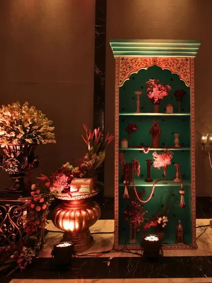 A hand-painted turquoise shelf filled with floral arrangements and traditional artifacts, serving as a beautiful and authentic decor piece for the Kashmir-themed event.