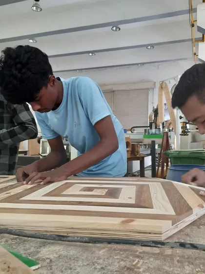 Students work on a decorative tabletop, carefully arranging pieces of different wood species to create a geometric inlay pattern.